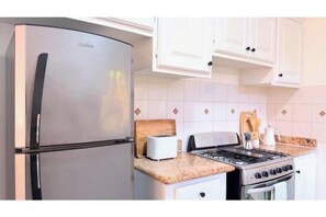 A kitchen with a stainless steel refrigerator, a gas stove, and white cabinets.