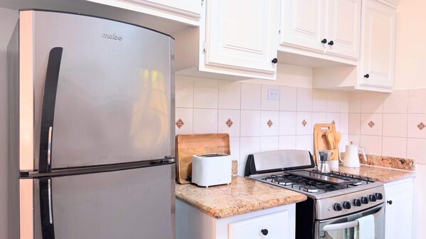 A compact kitchen with a stainless steel refrigerator, a toaster, a gas stove, and white cabinets.