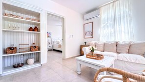A modern living room with a white sofa, a coffee table with a woven tray, and a bookshelf with decorative items.