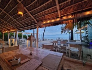 Een terras met overdekte rieten kap, sfeerverlichting en gedekte tafels voor gasten.