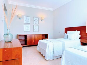 A hotel room with a wooden headboard, a bed with white bedding, a wooden nightstand, a wooden cabinet, and wall-mounted sconces.