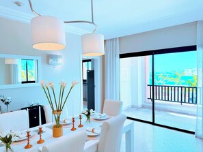 A modern hotel room with a balcony, a dining area with white furniture, and a view of the city. - Your Private Pool, Marina Resort & Grounds (Punta Cana)