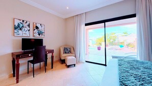 Une chambre d’hôtel comprenant un lit, un bureau avec une chaise, une télévision et une grande porte-fenêtre coulissante donnant sur un espace extérieur.