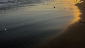 Une plage au coucher du soleil, avec le soleil qui disparaît à l’horizon de l’océan.