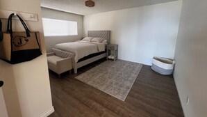 Une chambre à coucher avec un lit, une table de chevet, une commode et un grand sac accroché au mur.