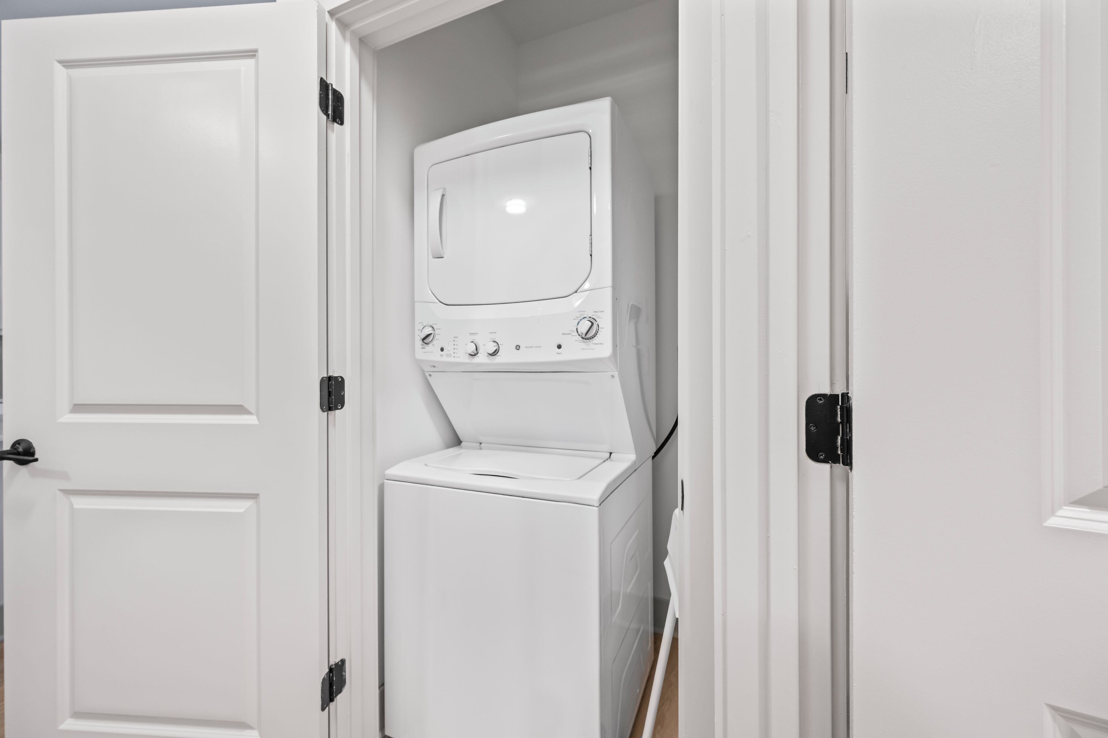 A laundry room with a stacked washer and dryer, a door, and a small window.