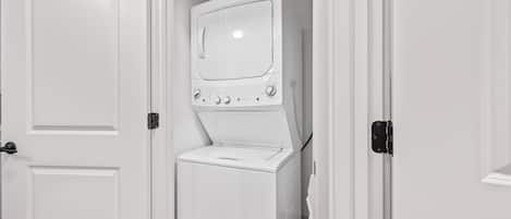 A laundry room with a stacked washer and dryer, a door, and a small window.