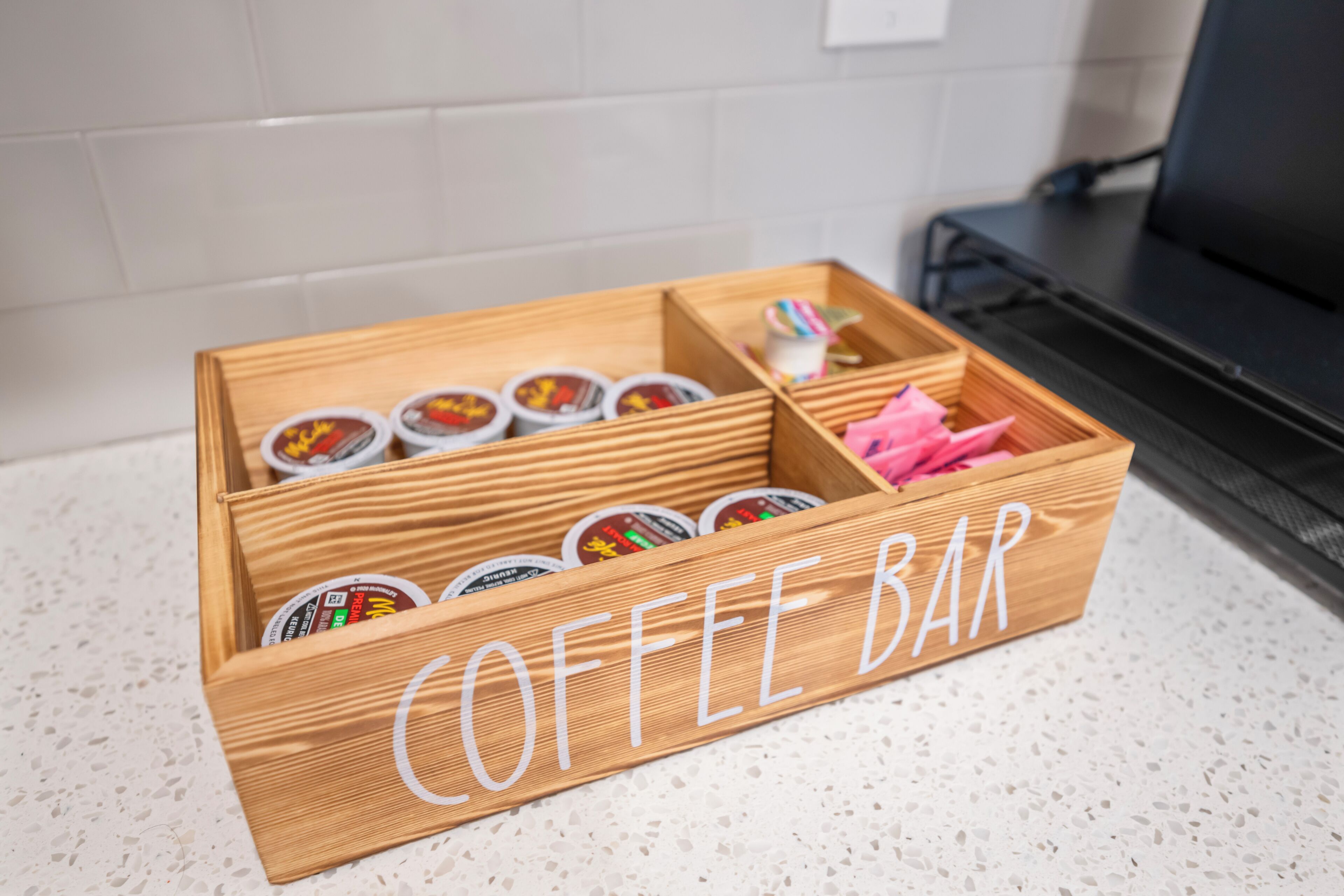 Un présentoir à café en bois, doté de compartiments pour ranger les dosettes de café et d’une boîte de mouchoirs rose.
