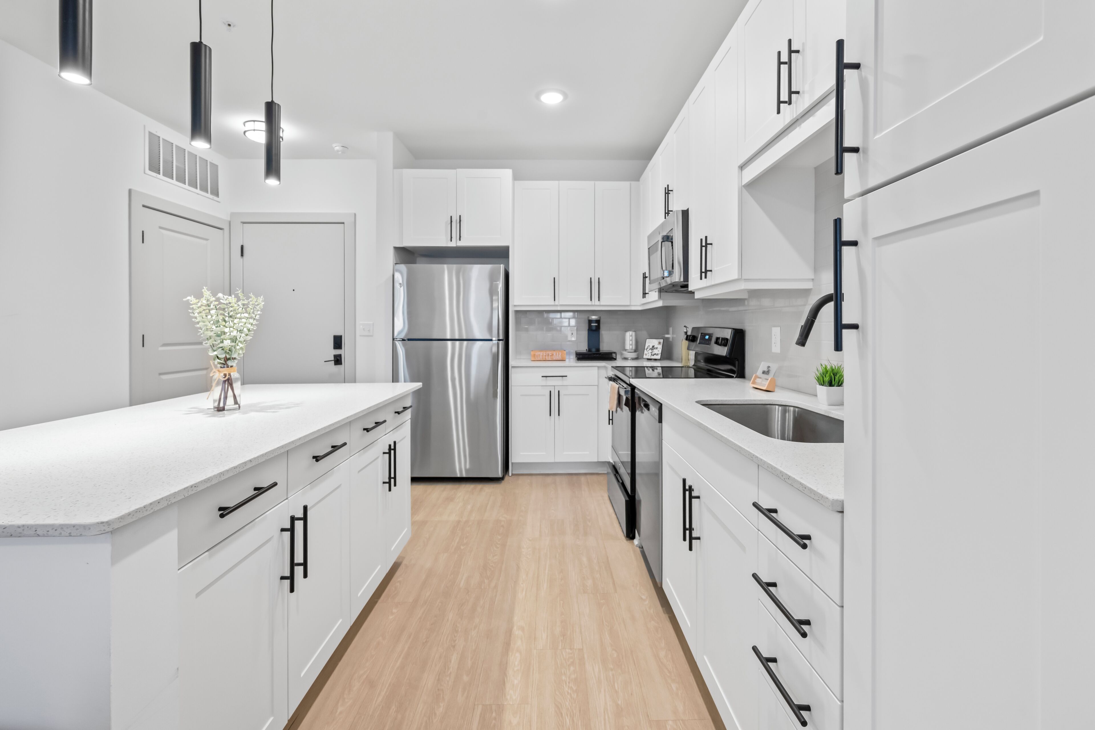 Une cuisine moderne avec des meubles blancs, des appareils en acier inoxydable et un plancher en bois.