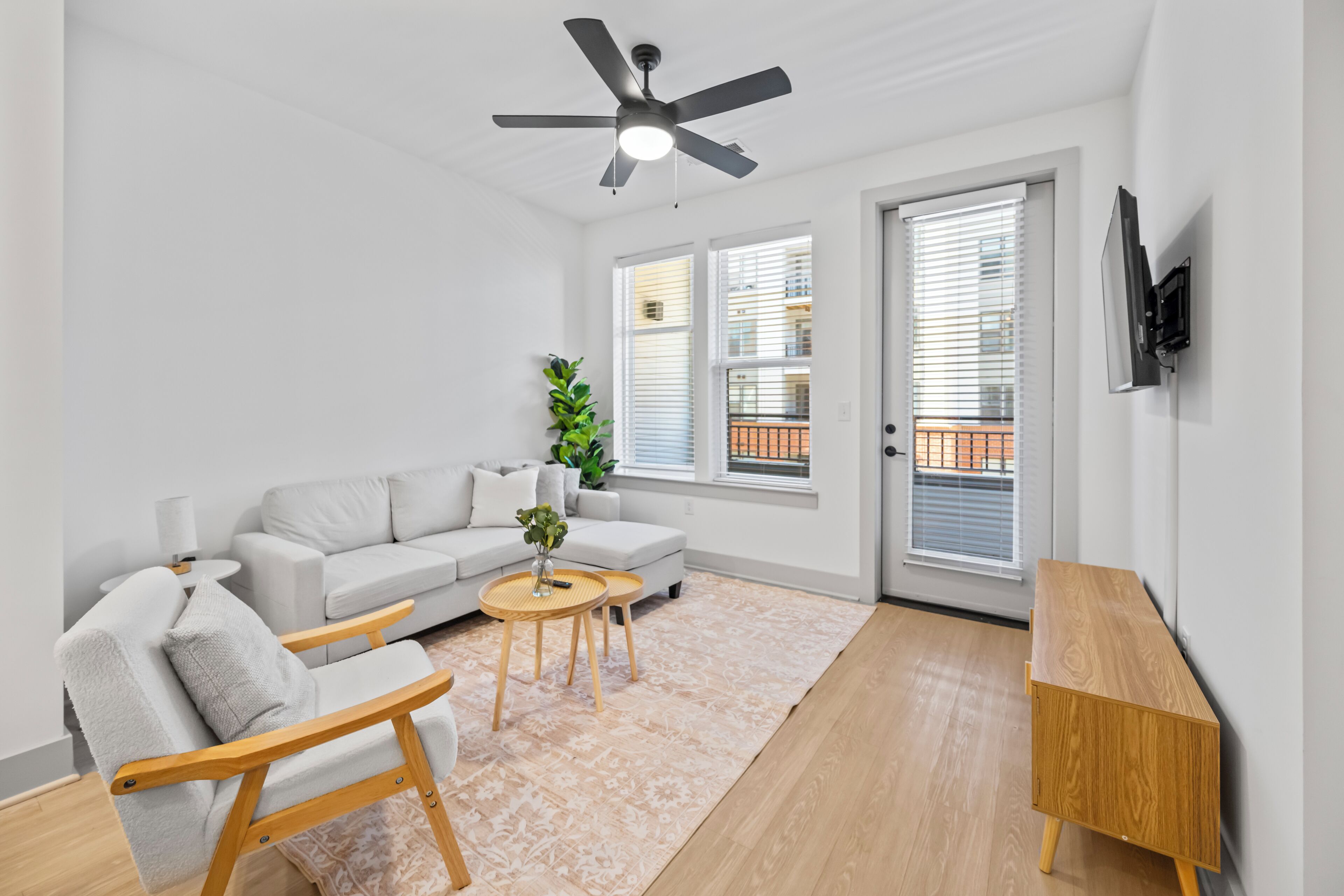 A modern living room with a white sofa, a wooden chair, a small round table, and a ceiling fan.