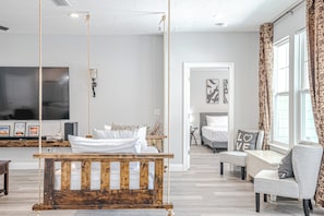 Un salon moderne avec une balançoire suspendue, un téléviseur, un canapé et un lit à l’arrière-plan.