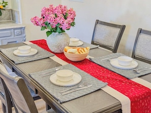 A dining table set with place settings, a bowl of bread, and a vase of flowers.