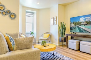 A modern living room with a sofa, armchair, round coffee table, and a large flat-screen TV mounted on the wall.