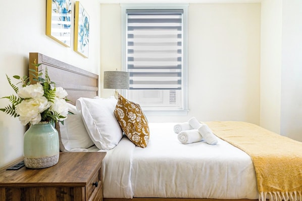 A neatly made bed with white bedding, a vase of flowers, and a lamp on a bedside table.