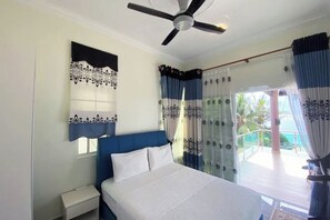 A bedroom with a bed, a nightstand, a ceiling fan, and a view of a balcony with curtains. - Che Beach House (Rusila)