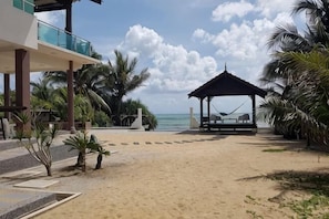 Une vue sur la plage avec un kiosque, des palmiers et un bâtiment doté d’un balcon.