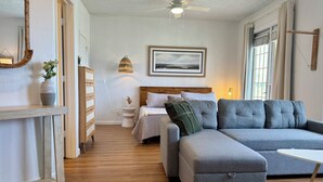 Un soggiorno moderno con un divano modulare grigio, una cassettiera in legno, un letto con testiera e un quadro appeso al muro.