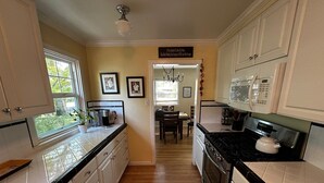 A kitchen with white cabinets, a black countertop, a stove, and a microwave. There is a window with a view of trees and a door leading to another room.