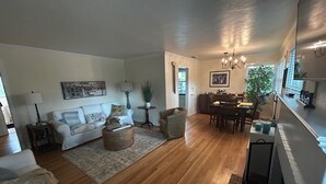 A living room with a sofa, a coffee table, a dining area with a table and chairs, and a chandelier.