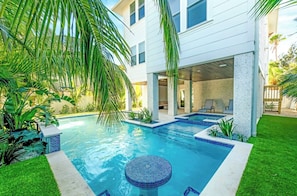 Ein modernes, zweistöckiges Haus mit Swimmingpool, Sitzgelegenheiten im Freien und üppigem Grün.