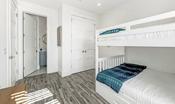Ein Schlafzimmer mit Etagenbett, Holzboden, weißen Wänden und einer Tür zu einem Badezimmer.