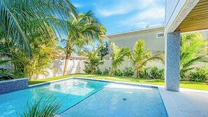 Una piscina con borde de azulejos, rodeada de palmeras y un césped cuidado.