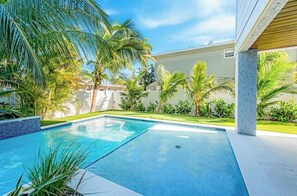 Una piscina con borde de azulejos, rodeada de palmeras y un césped cuidado.