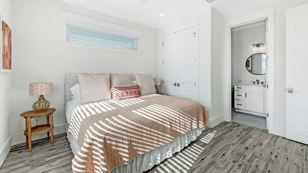 Un dormitorio con cama, mesita de noche, ventana con persianas, armario y baño con espejo.