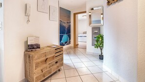 Un corridoio con un mobiletto in legno, un quadro incorniciato, una pianta in vaso e uno specchio appeso al muro.