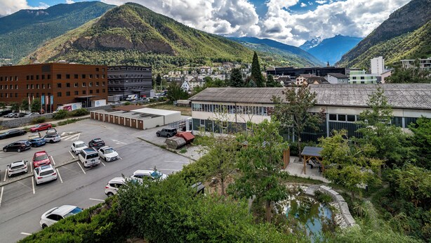 Un parcheggio con diverse auto, un edificio a tetto piatto e un paesaggio montuoso sullo sfondo.