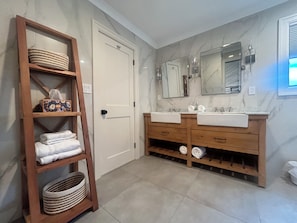 Ein Badezimmer mit zwei Waschbecken, einem Holzkosmetikschrank, einem großen Spiegel und einem Holzregal mit Handtüchern.