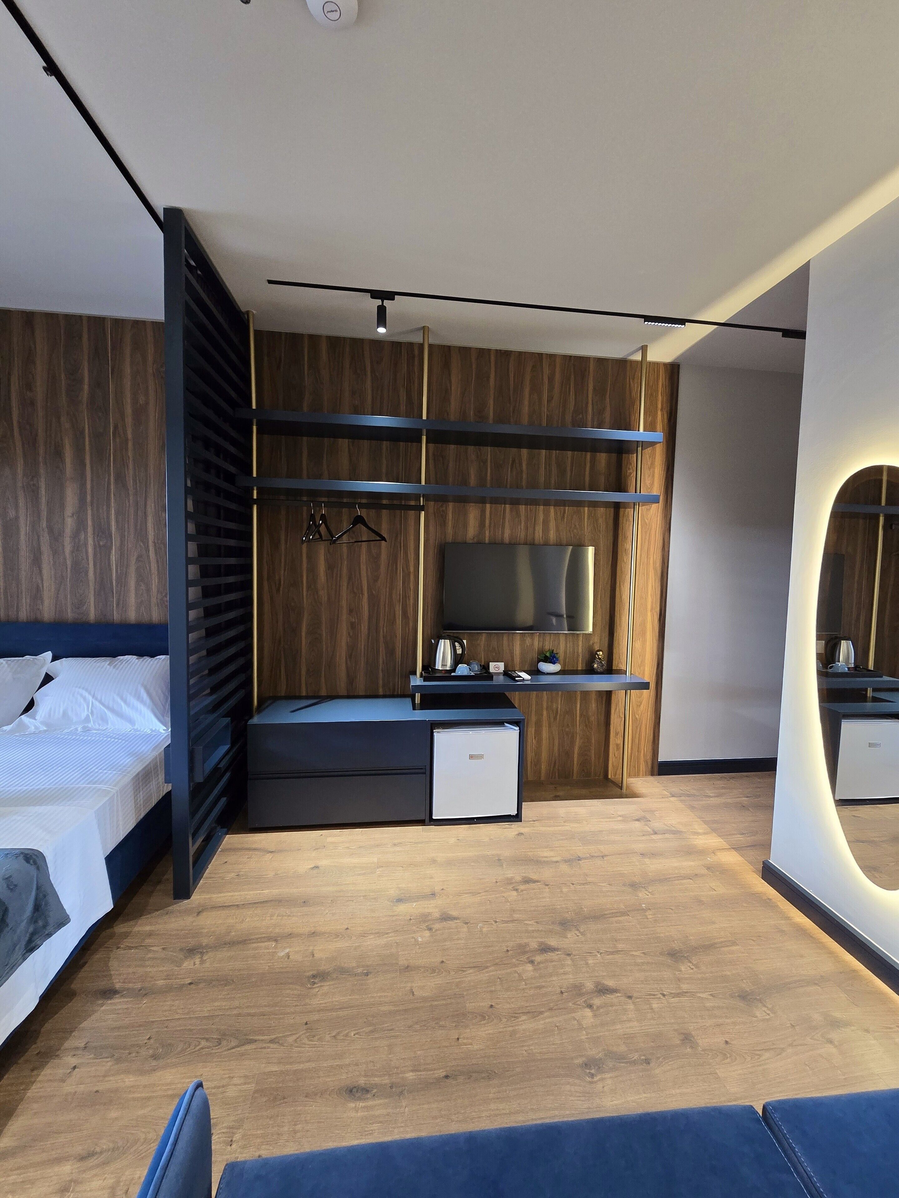 Un dormitorio moderno con cama, televisor, una pequeña kitchenette y suelo de madera.