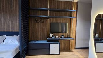Un dormitorio moderno con cama, televisor, una pequeña kitchenette y suelo de madera.