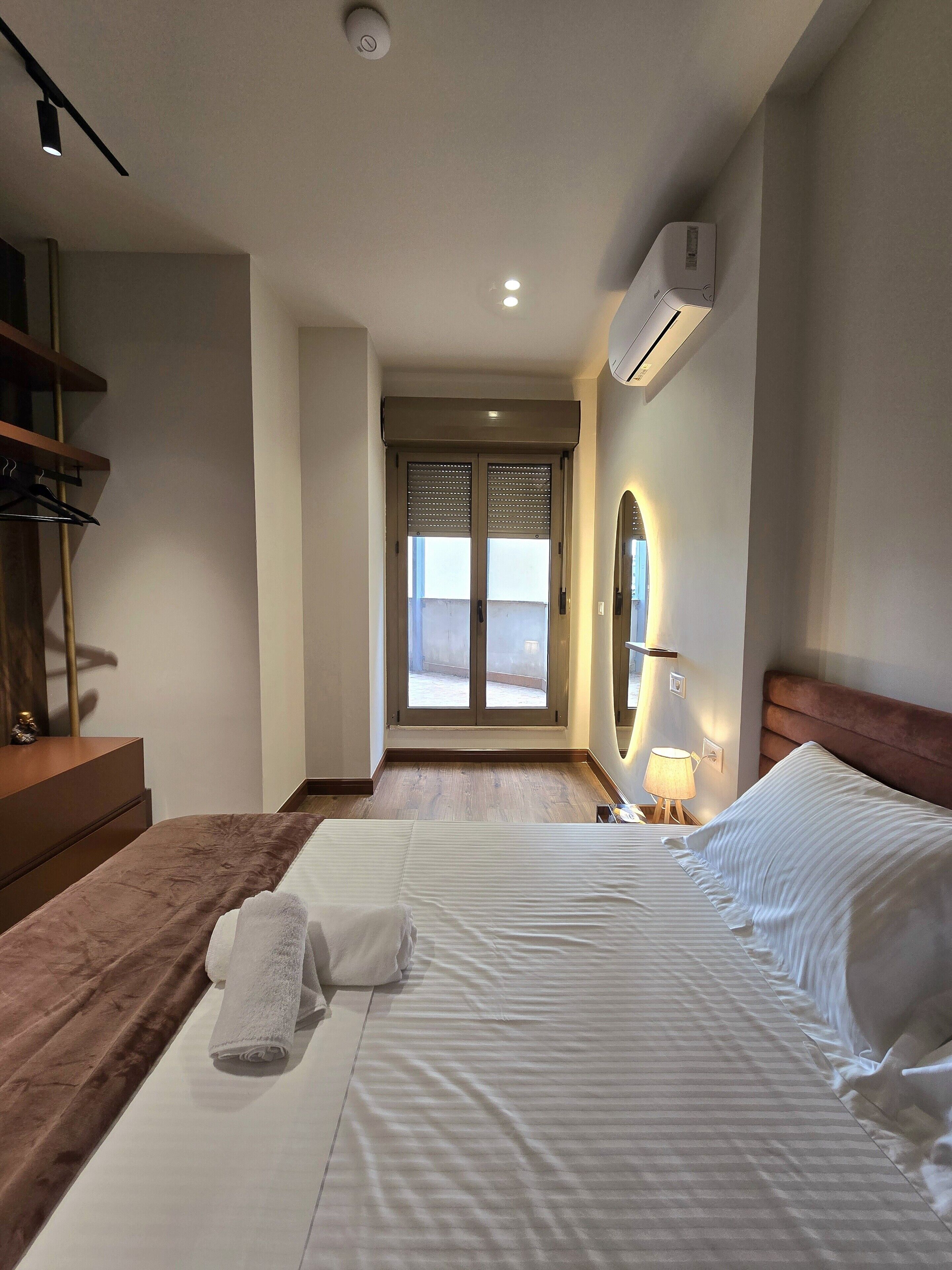 Une chambre d’hôtel avec un lit, une table de chevet, une lampe et une vue sur l’extérieur.