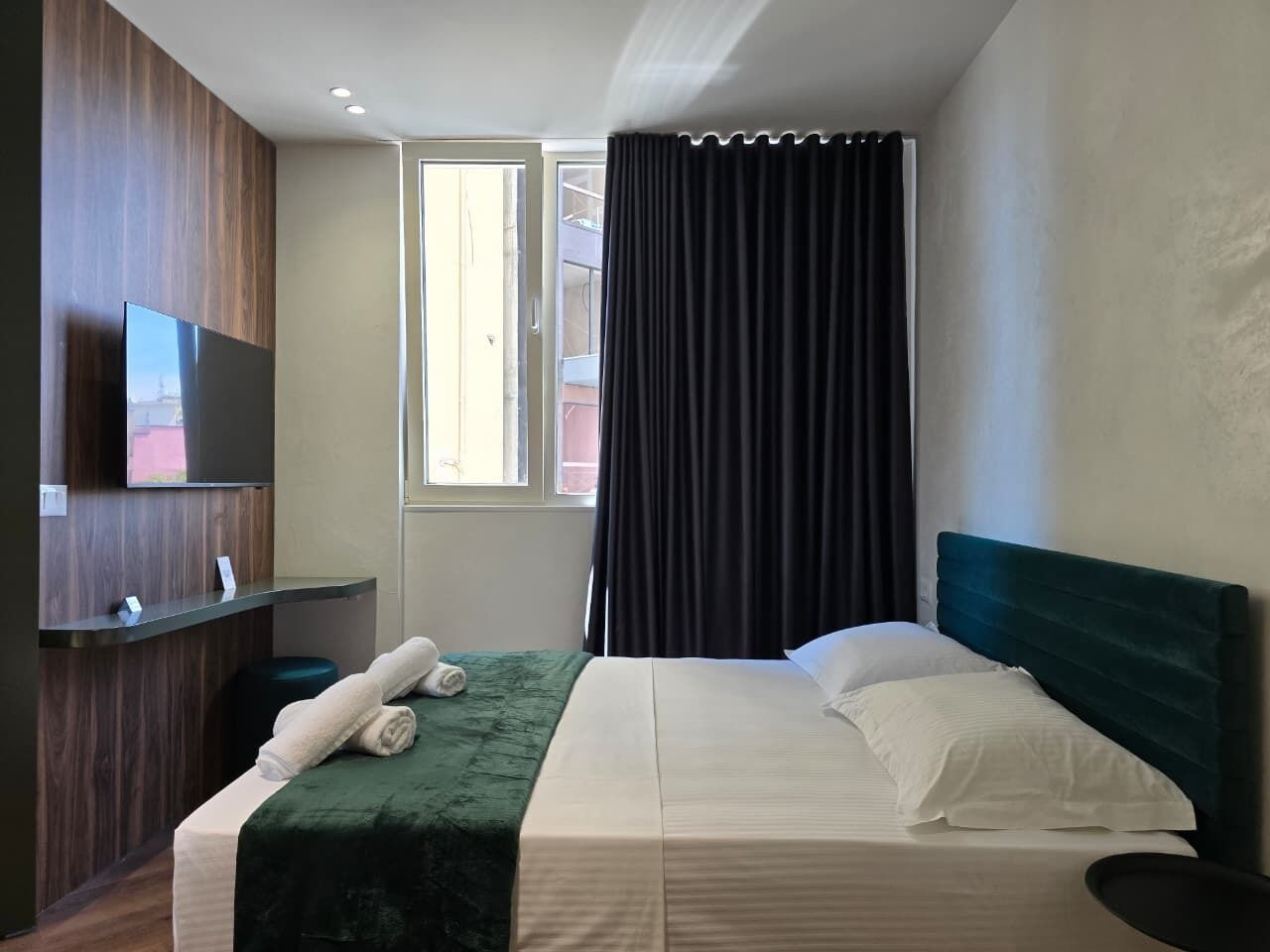 Une chambre d’hôtel avec un lit, un téléviseur à écran plat fixé sur un panneau en bois, une fenêtre avec des rideaux et une vue sur l’extérieur.