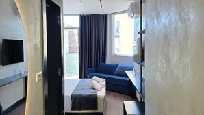 Una habitación de hotel moderna con una cama, un sofá azul, un televisor montado en la pared y un ventanal grande.
