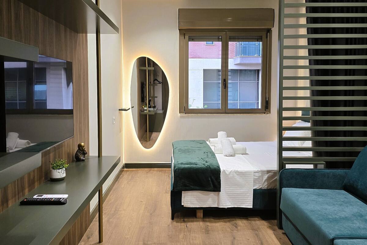 A modern hotel room with a bed, a sofa, a TV, and a small plant.