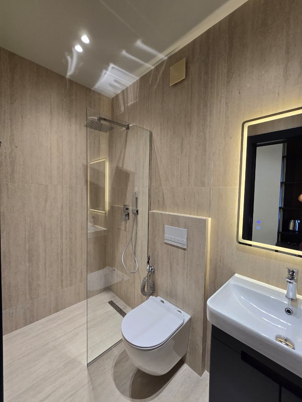 Un baño moderno con ducha envuelta en vidrio, inodoro y lavamanos con espejo.