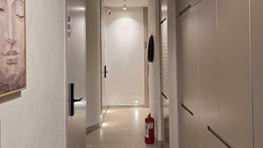 Un pasillo con suelo de madera clara, paredes blancas y una puerta al final.