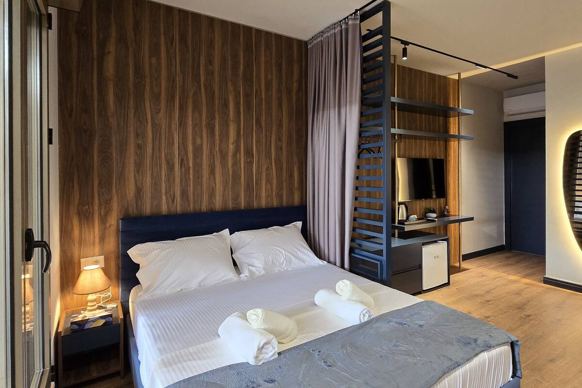 A modern hotel room with a large bed, a desk, and a built-in wardrobe.