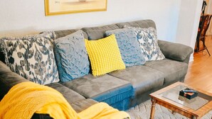 Un salon avec un canapé gris, un plaid jaune et une table basse.