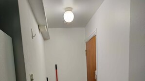 A narrow hallway with a wooden door at the end, a broom leaning against the wall, and a bucket on the floor.