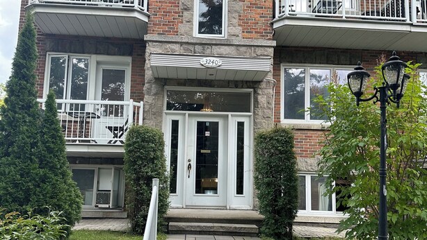 A two-story brick building with a stone entrance, a balcony on the second floor, and a small garden area with steps leading to the entrance.