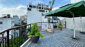 Una terraza en la azotea con plantas en macetas, un toldo verde y una barandilla de metal.
