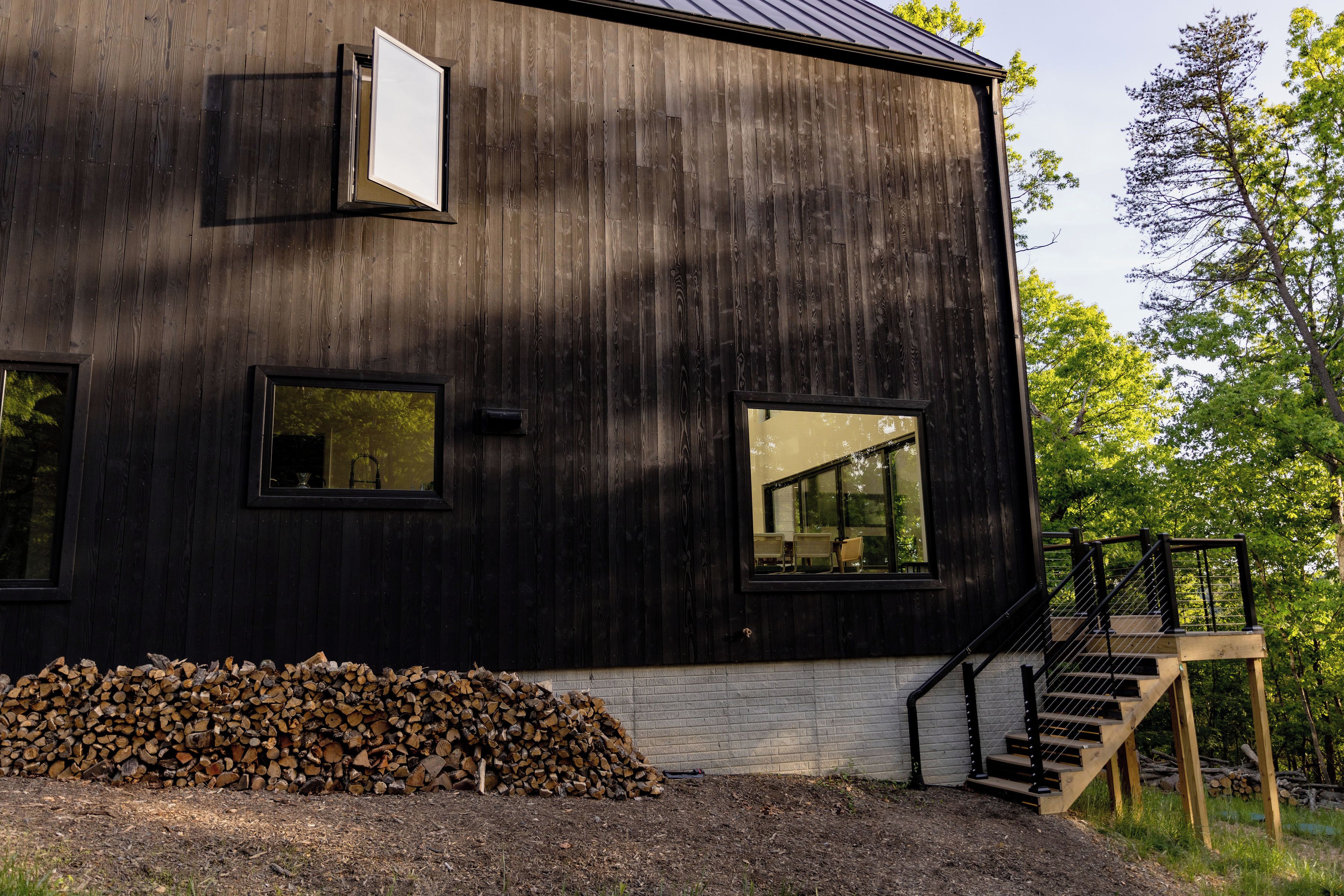 A modern wooden building with large windows and a staircase leading to a deck.