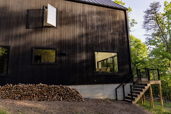 A modern wooden building with large windows and a staircase leading to a deck.