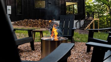 Un espace extérieur aménagé dans un style rustique, avec des fauteuils Adirondack, un foyer et un bâtiment en bois doté de grandes fenêtres.