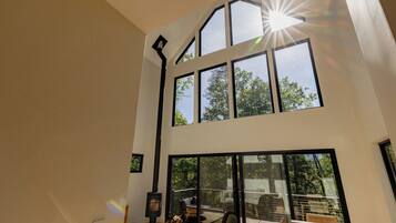 A high-ceiling room with a wood-burning stove, large windows, and a view of the outdoors.