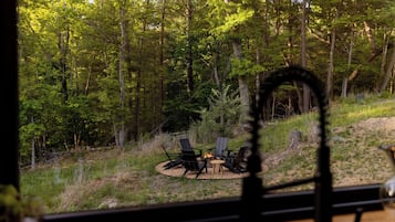 A forested area with a fire pit and chairs.