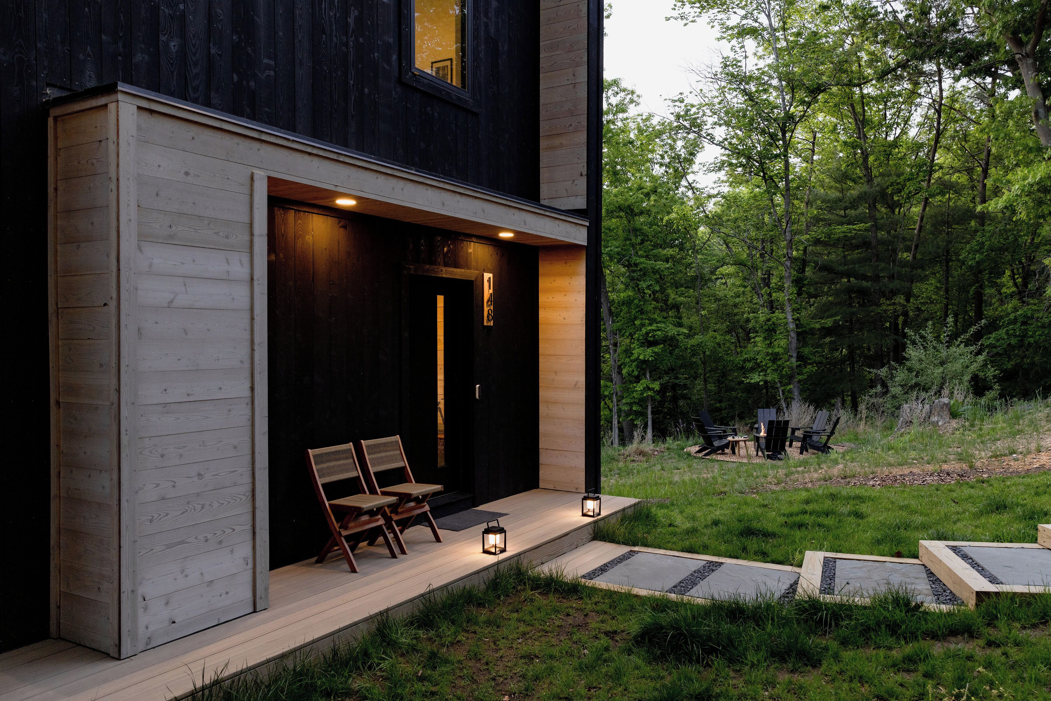 A modern house with a wooden exterior, a porch with two chairs, and a number sign.